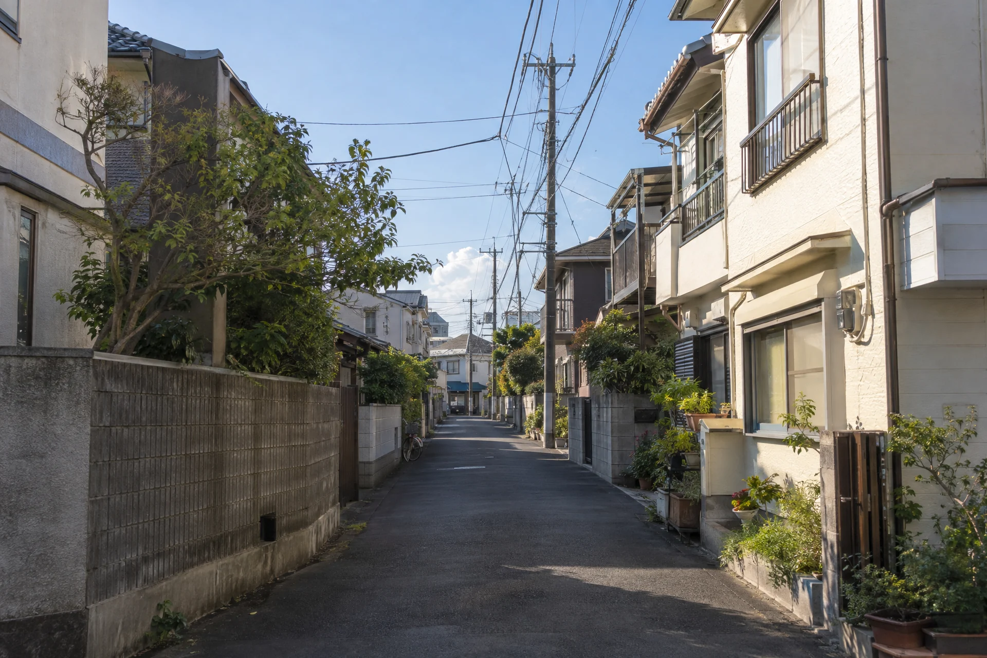 A quiet Japanese residential lane with cream houses, overhead wires, and long afternoon shadows